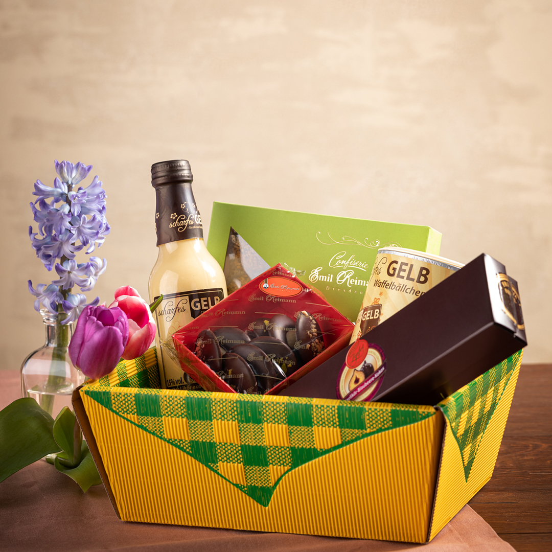 Geschenkpaket mit kleiner Flasche Eierlikör und Süßigkeiten. Daneben steht eine dekorative Blume.