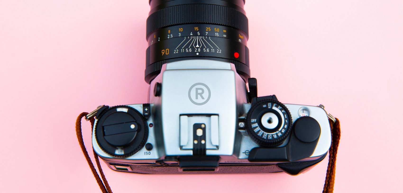 Analoge Kamera mit aufgedrucktem RIEGG-Logo vor rosa Hintergrund