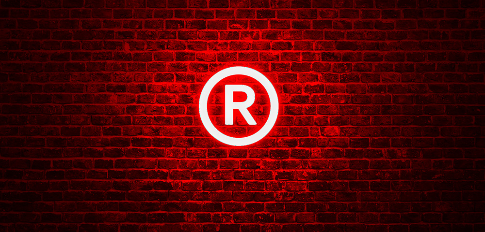 Das RIEGG-Logo hängt als leuchtend rotes Neonschild an einer Backsteinwand