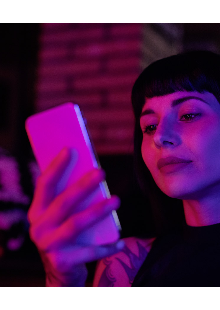 Junge Frau schaut aufs Handy im Neonlicht